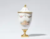 Werner & Mieth, A milk glass potpourri, White glass with polychrome painted decor, ormolu mountings, softwood. Tapering vase with a pierced domed lid. Decorated on one side with putti flying over clouds and playing with flowers. The upper rim with floral garlands, the lid with scattered flowers. The base, foot, shaft, inner ring of the lid and berry finial of bronze. Two restored chips to the rim of the lid. A reattached breakage to the upper back edge of the vase. H