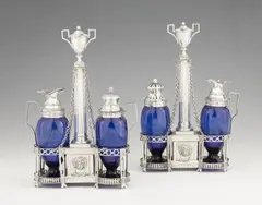 Jean Godet, A pair of Louis XVI Berlin silver cruets, Cruet stands on eight supports with pierced holders for two blue glass vessels and central columnar handles. One with silver-mounted oil and vinegar bottles, the other with a mustard pot and spice cruet. H