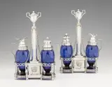 Jean Godet, A pair of Louis XVI Berlin silver cruets, Cruet stands on eight supports with pierced holders for two blue glass vessels and central columnar handles. One with silver-mounted oil and vinegar bottles, the other with a mustard pot and spice cruet. H