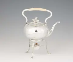 Johann David Hertel, A Berlin silver tea kettle and rechaud., In a pressed spherical form, on a three-legged rechaud with adjusted burner. The body with classicistic engraving and relief decoration; the curved folding handle with ivory grip, the cover with a plastic hippocamp as knob. H