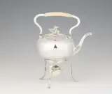 Johann David Hertel, A Berlin silver tea kettle and rechaud., In a pressed spherical form, on a three-legged rechaud with adjusted burner. The body with classicistic engraving and relief decoration; the curved folding handle with ivory grip, the cover with a plastic hippocamp as knob. H