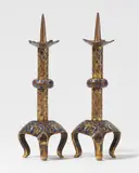 Limoges early 13th century, Two early 13th century Limoges enamel candlesticks, Cast bronze with engraved, chased, gilded and enamelled decoration. Matching pair of identical candlesticks. The triangular plinths resting on scrolling feet and decorated with gold tendril motifs on dark blue enamel ground. The slender shafts with gilded rhombus patterns and divided by round, compressed nodules decorated with corresponding tendrils. The undersides of the five-sided drip pans with enamelled many-pointed star motifs. This pair of candlesticks is highly comparable to an example in the Musée de Cluny in Paris which Marie-Madeleine Gauthier (op. cit.) has also classified as a 13th century work from Limoges. The surfaces slightly abraded. Minor losses to the enamel. Height 26 and