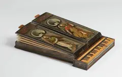 Nuremberg, A small portable organ, a so-called “bible regal” from Berlaymont Convent in Brussels, Oil paint on softwood, resonators, pipes and brass registers. The keyboard made from boxwood veneer on oak. The two folding bellows made from parchment, each with six pleats. An organ designed to be placed on a table constructed from three parts: An oblong corpus comprised of the two bellows placed on top of one another with a hollow section on the inside to hold the keyboard. The moulded edges of the corpus of ebonised wood, the upper faces of the bellows each decorated with a full-figure depiction of an angel making music within a rounded arch with shell motifs en grisaille. The edge of the keyboard painted on three sides, the upper section with a band of foliage, the sides with winged angel's heads. Dimensions when extended H 12.5, W 61.5, D