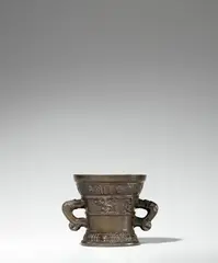 Werkstatt Hachmann, A small Hachmann mortar, Golden brown cast bronze with vivid chocolate brown patina. The display side decorated with a vacant coat-of-arms supported by winged demi-figures. With two wide banderoles below the rim and above the base inscribed in Gothic minuscule: “int iaer ous heren m vc lxxiii” and “myn hape steit allein in godt”. With two zoomorphic handles. H 10.8, D