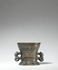 Werkstatt Hachmann, A later Hachmann mortar inscribed “IN DEO SPES MEA”, Golden brown cast bronze with uneven brown patina. The display side decorated with a vacant coat-of-arms supported by winged demi-figures. With two wide banderoles below the rim and above the base inscribed in Gothic minuscule and Latin capital letters: “int iaer ons heren m vc lxxxiii” and “IN DEO SPES MEA”. The handles formed as dolphins. H 13, D