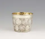 Jochim Sigismund Meissner, An early Berlin silver coin beaker, Parcel gilt silver beaker with a moulded rim. Decorated with embossed and chased acanthus foliage surrounding 20 17th century brandenburg and Brunswick-Lüneburg coins. The base inset with a coin dated 1698. With a later dedication engraving to the underside “:v:K: G.G.v.S. d. 10ten July 1767“. H