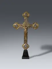 Maasland, A 14th century processional cross, presumably Maasland, Cast bronze on a wooden base with engraved brass mountings and remains of original gilding. The Corpus Christi is here placed separately against the square shaped centre of the cross and the four symbols of the evangelists against the quatrefoil terminals. The front of the cross is engraved with the Lamb of God in the centre and stylised tendrils on the beams. The engravings of the reverse repeat the symbols of the evangelists and tendrils whilst the centre shows the Veil of Veronica with the Vera Icon. The horizontal beam behind the Corpus reattached with solder. With dents and abrasions. Mounted on a wooden plint
