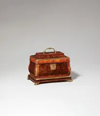 A bombé form box by Abraham Roentgen, A bombé form box by Abraham Roentgen, Burr walnut, rosewood and cherry veneer on oak and solid cherry with fire-gilt bronze, brass and steel mounts. Of rectangular shape with hinged top and handle. The larger base resting on four curved bracket feet. A finely engraved cartouche-shaped lock plate opens by pushing a button which activates a spring mechanism to reveal the keyhole. The box contains a shallow removable tray with two cherry wood compartments (with a horizontal crack) above a large unveneered compartment and a shallow secret compartment in the right side of the base which can be opened by pushing a rectangular button placed int he inner right side. All faces decorated with finely grained veneers framed by brass and pale rosewood stringing. The convex edges and moulded base accentuated by brass fillings. The lid inset with a small brass cartouche engraved with a dragon. H 18.1, W 23.5, D