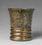 An early Grassmayr mortar dated 1647, An early Grassmayr mortar dated 1647, Golden brown cast bronze with slightly silvery shimmering patina. The display side decorated with a row of putto heads, grotesques, vases of flowers, grapevines, lion mascarons and a central medallion. Inscribed above and amidst the depiction with the owner's monogram and the date "M A B 1647". Scroll handle with a figurehead. Casting faults to the base, the interior discoloured. H 17.2, D