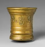 A Grassmayr mortar dated 1672, A Grassmayr mortar dated 1672, Golden yellow cast bronze with natural patina. The display side decorated with a frieze of foliate grotesques, sage leaves, and poppy flowers surrounding a central oval medallion depicting the Virgin and Child. With the date “1672” in relief. The handle formed as a dolphin. The base rounded due to usage. H 17.9, D