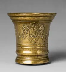 A Grassmayr mortar dated 1676, A Grassmayr mortar dated 1676, Golden yellow cast bronze with shimmering natural patina. The display side decorated with sage leaves, bunches of flowers and a cherub's head surrounding an oval medallion depicting the Virgin Mary and dated “1676”. The C-shaped handle formed as a dolphin. H 14.1, D