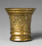 A Grassmayr mortar dated 1676, A Grassmayr mortar dated 1676, Golden yellow cast bronze with shimmering natural patina. The display side decorated with sage leaves, bunches of flowers and a cherub's head surrounding an oval medallion depicting the Virgin Mary and dated “1676”. The C-shaped handle formed as a dolphin. H 14.1, D