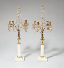 Werner & Mieth, A pair of Berlin Neoclassical candelabra, Designed as a pair of slender metal-mounted white marble columns supporting gilt bronze and metal arms terminating in scrolls beneath the pierced drip pans, hung with cut glass festoons and surmounted by pinecone finials. A repaired breakage through one arm. H 68 and