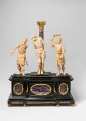 after François Duquesnoy Alessandro Algardi, A 17th century Italian carved ivory depiction of the Flagellation, copy after Alessandro Algardi or François Duquesnoy, Carved ivory and ebony set with amethyst, jasper, and other coloured gemstones, ormolu mountings. Three-figure group carved in the round on a rectangular plinth and a trompe l'oeil earth mound base. Christ depicted in the centre slightly elevated and tied to the column, flanked by two men in Roman legionary uniforms beating him with ropes and switches. The plinth is decorated with pietra dura, the column with stone veneer, the lisenes and capital of gilt bronze. The composition of this flagellation group, which is usually carried out in bronze, can be traced back to two leading personalities of the Roman Baroque: Alessandro Algardi and François Duquesnoy. Whereby Jennifer Montagu was able to specify this attribution in her publications from 1967 and 1985 (op. cit). The present version differs from the ascription to Algardi, as the two soldiers are not shown in loincloths like Christ, but instead wear tunics and leggings. Christ and the soldier on the left also show more connection to one another through the position of the heads and through eye-contact than in other examples of th In good overall condition. Wear to the ivory. H 73.3, W 58, D