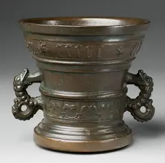 A dated Hachmann mortar, A dated Hachmann mortar, Cast bronze, the golden brown patination presumably re-applied and with traces of green corrosion. A fleur-de-lys band surrounding the lower border beneath a vacant shield supported by two winged half-figures. A broad banderole around the rim inscribed "anno domini MCCCCCXLVI". The handles formed as two-headed dragons. H 13.9, D