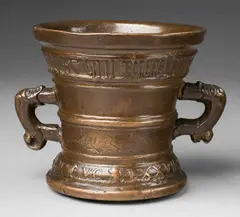 A small dated Hachmann mortar, A small dated Hachmann mortar, Cast bronze with brown lustrous natural patina. Decorated with a vacant heraldic shield supported by two winged half-figures. A broad banderole below the rim inscribed in Gothic minuscule "anmicis syn huisfrou derich franchen". Dated above the base "ANNO DOMINI MVCLXXVII". A horizontal crack to the lower section. H 11.6, D