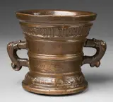 A small dated Hachmann mortar, A small dated Hachmann mortar, Cast bronze with brown lustrous natural patina. Decorated with a vacant heraldic shield supported by two winged half-figures. A broad banderole below the rim inscribed in Gothic minuscule "anmicis syn huisfrou derich franchen". Dated above the base "ANNO DOMINI MVCLXXVII". A horizontal crack to the lower section. H 11.6, D