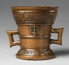 A dated Hachmann mortar, A dated Hachmann mortar, Cast bronze with slightly mottled honey coloured patina. Two banderoles surround the rim and base, the upper inscribed in Gothic minuscule "jan martens lennchen syn huisfrouw", and the lower dated "ANNO DOMINI 1581". Surface of the vessel divided by horizontal mouldings. Decorated with a heraldic shield flanked by two winged half-figures avers and a worn ornamental motif beneath a winged putto head to the reverse. Rectangular Gothic handles. H 16,5, D