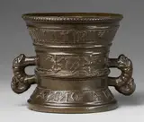 A small dated Hachmann mortar with lion mascarons, A small dated Hachmann mortar with lion mascarons, Cast bronze with dark brown patina. With a central lion mascaron flanked by two lions rampant to the front and a shield with the owner's mark supported by two winged half-figures to the reverse. The rim with a broad banderole in Gothic minuscule "willem van geulluch eyeniken s h f", the base inscribed in majuscule "ANNO DOMINI 1601". Dolphin handles. Minor traces of green corrosion. H 12.4, D