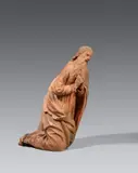 Probably Landshut circa 1520, A clay figure of Saint Joseph from a Nativity scene, probably Landshut, circa 1520, Fired clay, worked three-quarters in the round, the reverse deeply hollowed out. Minimal remains of former polychromy. A figure of a kneeling bearded man with his hands folded in prayer, facing to the right and leaning slightly forward. The piece is presumably a figure of Saint Joseph from a Nativity scene. The size of the figure, designed for a slightly lowered viewpoint, and the pronounced curve of the spine indicate that it was designed to be placed in the tympanon of a church portal. The composition of this work displays generously folded drapery, and detailed expressive physiognomy and finely carved hair. This South German work probably originates from Landshut, where there were workshops producing large-format clay sculptures for use in architecture in the late Gothic period. A crack to the neck. Wear with losses, especially to the right shoulder, the lower left edge, and the back right hem of the robe. Some places overworked in clay and plaster. Mounted on a wooden plint