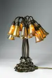 A Tiffany Studios Twelve-light Pond Lily Lamp by Tiffany Studios, Favrile glass shades with gold lustre, brown patinated bronze base, original mountings. Including one later lamp shade. , sold Nov 2018
