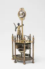 Hanns Buschmann, An Augsburg figural clock with an African man and an ostrich, Gilt bronze and copper, engraved silver, brass. Later day-running movement with hourly striking to a bell. The movement and figures attached to an upper panel supported by six columns. Next to a diminutive ostrich, an African man dressed as a Roman soldier holding a sabre stands with his hand resting upon a palm tree supporting the globe-shaped clock. The equator forms the hour aperture, with a single stationary hand dropping down from a wreath surrounding the globe. Engraved to the upper panel: Hannß Buschmann A. (presumably originally the plate). The movement, arrow, and lower panel later additions. H