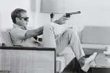 John Dominis, Steve McQueen aims a pistol in his living room, CA, 1963, Posthumous gelatin silver print, printed