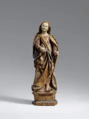 Bavaria circa 1500, A Bavarian carved limewood figure of a female saint, circa 1500., Carved in the round. With extensive remains of the presumably original polychromy.. A standing, full-figure depiction of a saint on a moulded hexagonal plinth, designed for a frontal viewpoint. The attribute in her extended left hand is lost. The Saint's face is framed by long waves of hair, which are depicted in detail to the front and back of the work. The figure's sculptural quality is largely defined by the cloak drawn across her body, which shows a rich and partially undercut play of drapery throughout. The sculpture originates from Landshut in Lower Bavaria. Wear with very minor losses