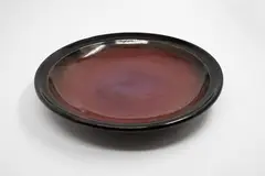 Michael Lucas, Red platter, stoneware with tenmoku glaze giving to a pool of bright red glaze to the centre