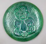 Crown Lynn Wharetana Ware, 'Hei Tiki' wall plaque, green glazed ceramic (with hanging wire through suspension holes to foorim)