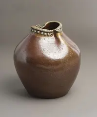 Barry Brickell, Large 'Fatso' vase, stoneware with speckled persimmon glaze thinning around the rim, the rim pinched on two sides with stylized characterful beak forms and applied rivet detail