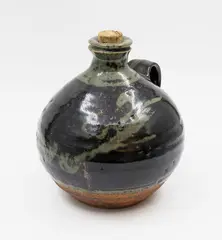 Wine flagon by Len Castle, stoneware of squat ovoid form, celadon wax resist blossom design under tenmoku glaze, original cork stopper, sold Feb 2026