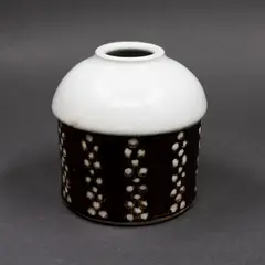 Domed cylinder vase by Graeme Storm, porcelain, the body decorated with bands of white dots on a dark brown ground, very pale celadon glaze to the domed top, offered May 2025