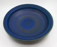Large wall charger by Graeme Storm, stoneware with rich matt blue barium glaze, thinning to pale green to the rim, fitted with hanging wire, offered May 2025