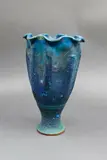 Fluted stoneware vase by Graeme Storm, of tapered form with a frilled flared rim and lobed sides, rich blue and green copper carbonate glaze, offered May 2025