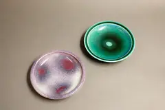 Two pin dishes by Graeme Storm, comprising a stoneware dish with gloss aqua green glaze, and a porcelain dish with purple and pale blue jun glaze, offered May 2025