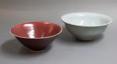 Two Chinese style bowls by Graeme Storm, comprising a porcelain bowl with rich copper red glaze, and a stoneware bowl with pale celadon glaze, offered May 2025