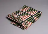 Mosgiel Woollens Ltd, Manatunga travel rug, decorated with a tukutuku panel pattern in olive green, brown, black and white
