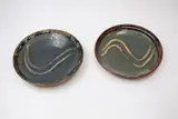 Barry Brickell, Two similar stoneware dishes, with wax resist gestural decoration on a blue ground, rim detailed in tenmoku glaze