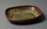 Len Castle, Large stoneware platter, ash and tenmoku glazed stoneware, the deep well walls impressed with various stamps, some attributed to Theo Schoon, impressed rope pattern to the centre (crack)