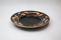 Large dish by Peter Collis, with shiny black glaze, the wide straight rim decorated with gold and red gestural design, sold Feb 2024