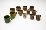Collection of 11 cups and a small jug by New Zealand Studio Pottery, including a set of four Paula King tenmoku glazed cups; a set of five Ian Firth mottled grey cups; a green glazed Elizab, offered Feb 2024