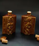 Parker Potteries, A pair of Lincoln Wines bottles, decorated with a tiki figure on one side and a manaia on the reverse, ceramic cork stopper