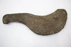 Patu Okewa, Rare Chatham Island curved stone okewa [hand club], bird shape, oval cross section. Worn oval knob on the top of the handle. Surface pitted and some flake scars, surfaces worn.