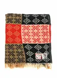 Onehunga Woollen Mills, Te Ariki travel rug, with a tukutuku panel pattern in red, black, white, and light brown