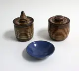 Elizabeth Lissaman, Two preserve pots and a small dish, the lidded pots banded with white and cream slip decoration, the dish with speckled blue glaze