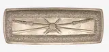 Anton Teutenberg, A silver belt buckle, decorated with crossed rifles and taiaha within a foliate scroll boarder.