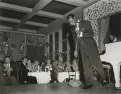 Sid Avery, Nat "King" Cole performs at Ciro's Night Club. In the audience Jack Palance (left) and Gig Young (right), 1954, silver gelatin photograph, ed. 22/70