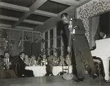 Sid Avery, Nat "King" Cole performs at Ciro's Night Club. In the audience Jack Palance (left) and Gig Young (right), 1954, silver gelatin photograph, ed. 22/70