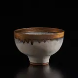 Footed bowl by Lucie Rie, circa 1974, Stoneware, grey glaze with blue band and running golden manganese rim, sold Dec 2024